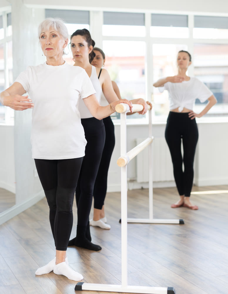 Elderly woman practicing ballet moves at barre during group class