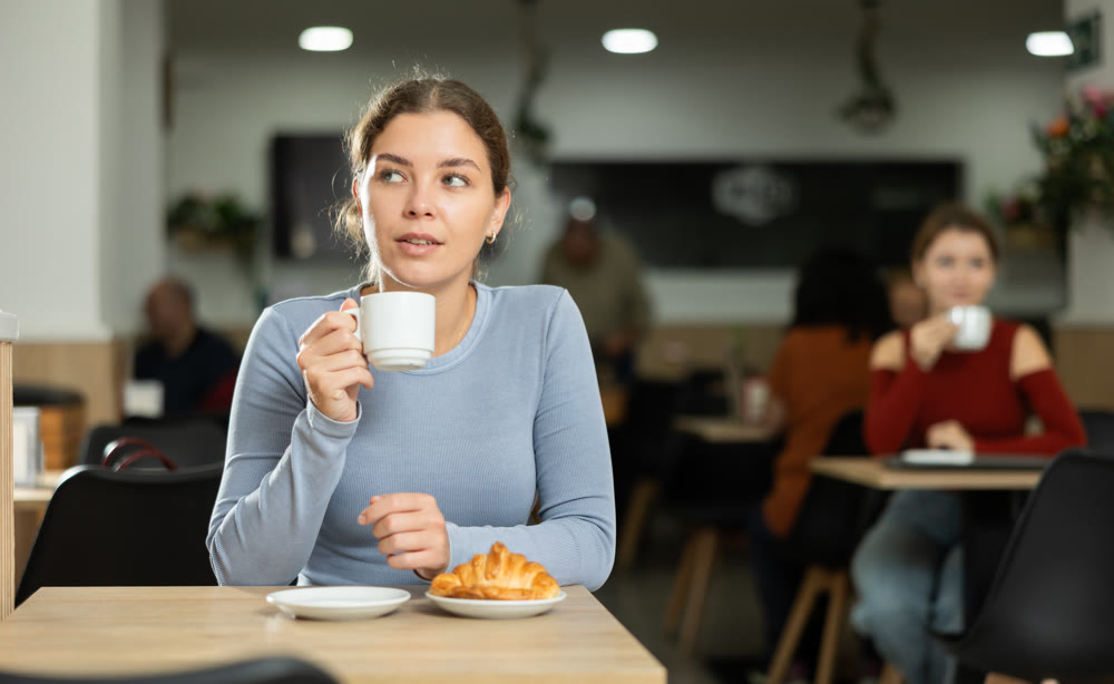 Young girl enjoying coffee and croissant in cafeteria