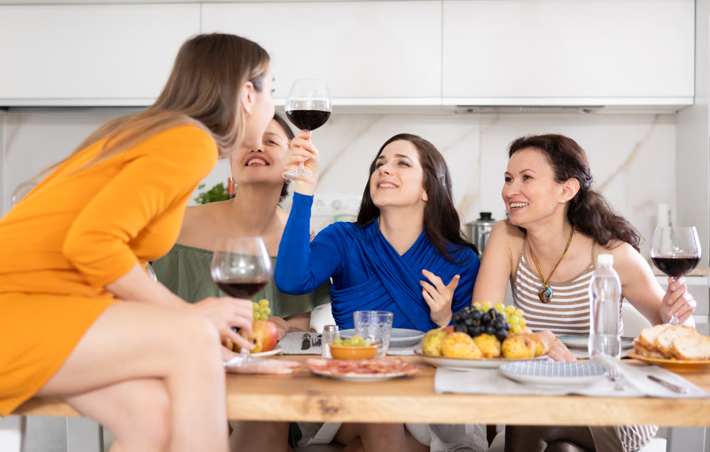Girlfriends drinking wine and having conversation over dinner at house party
