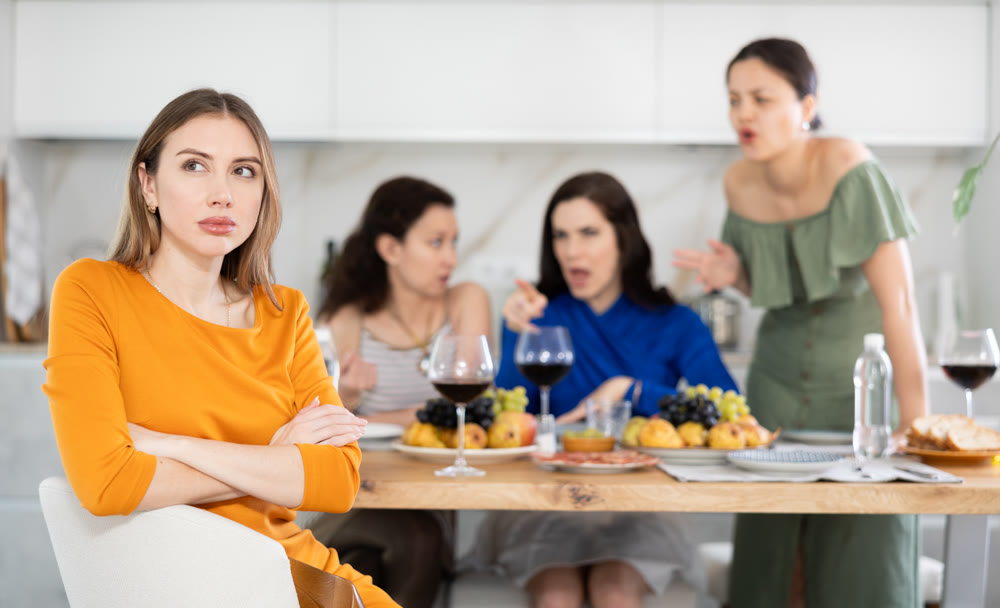 Upset woman listening to criticism from friends during home gathering