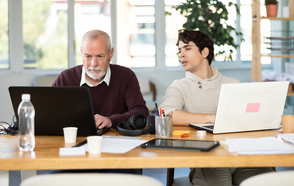 Two male manager work on laptops in modern company office