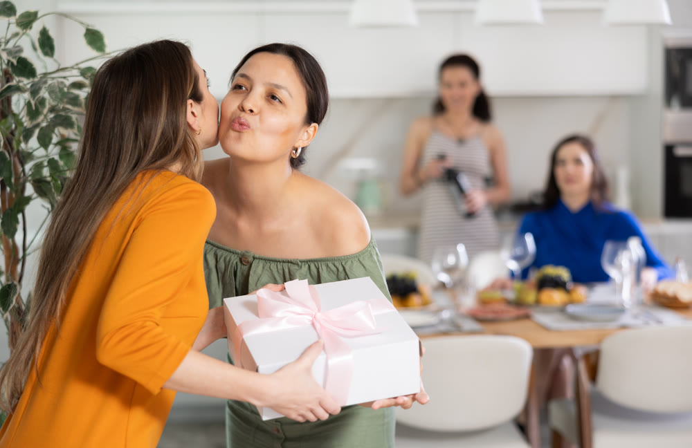 Smiling Asian woman kissing bestie arriving for friendly party