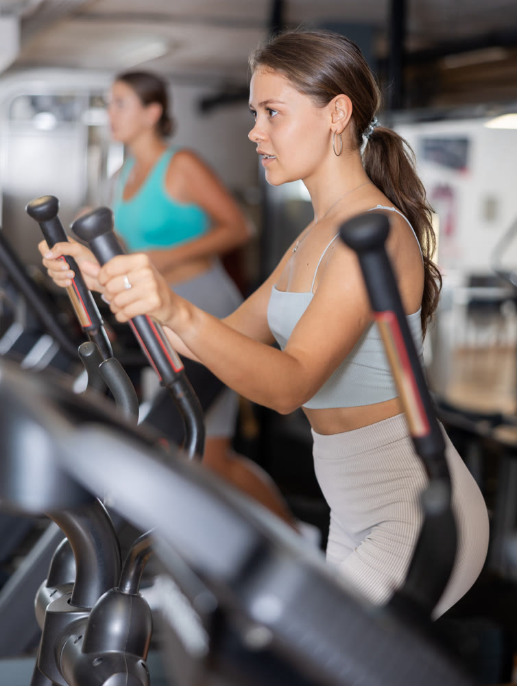Portrait of sporty woman doing cardio workout on elliptical cross trainer at fitness center