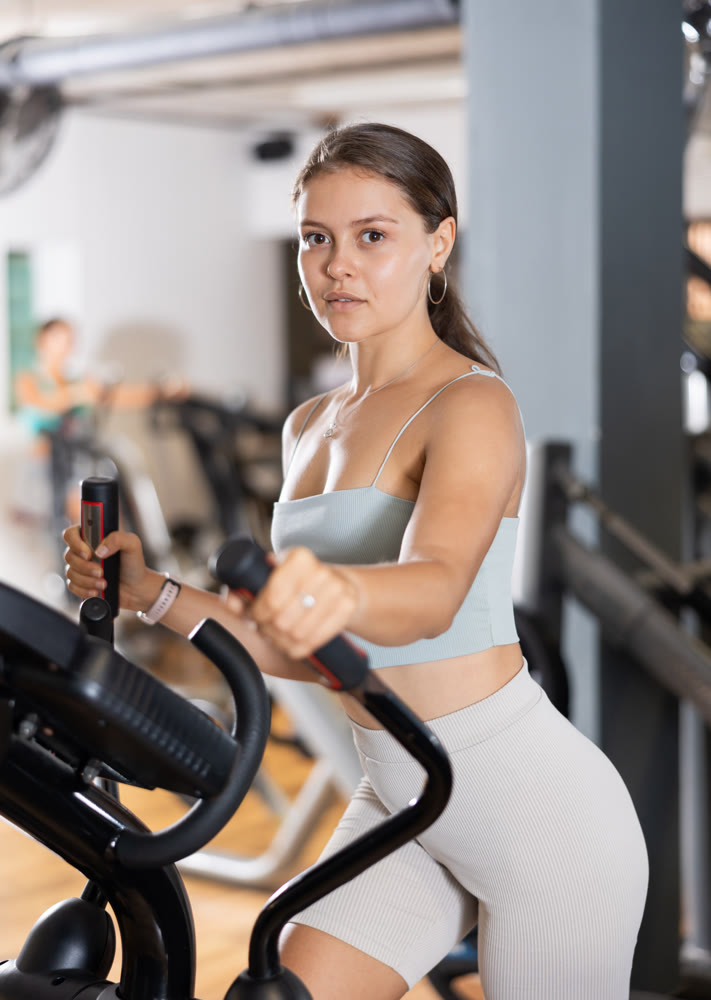 Sporty girl working out on elliptical machine in gym. Healthy active lifestyle concept