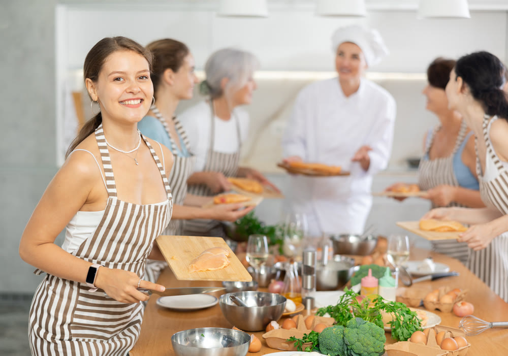 Girl at group class of culinary school cuts up chicken and prepares low-calorie diet lunch