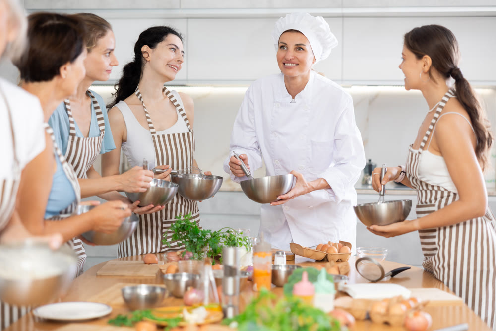 Young female cook holding bowl and whisk