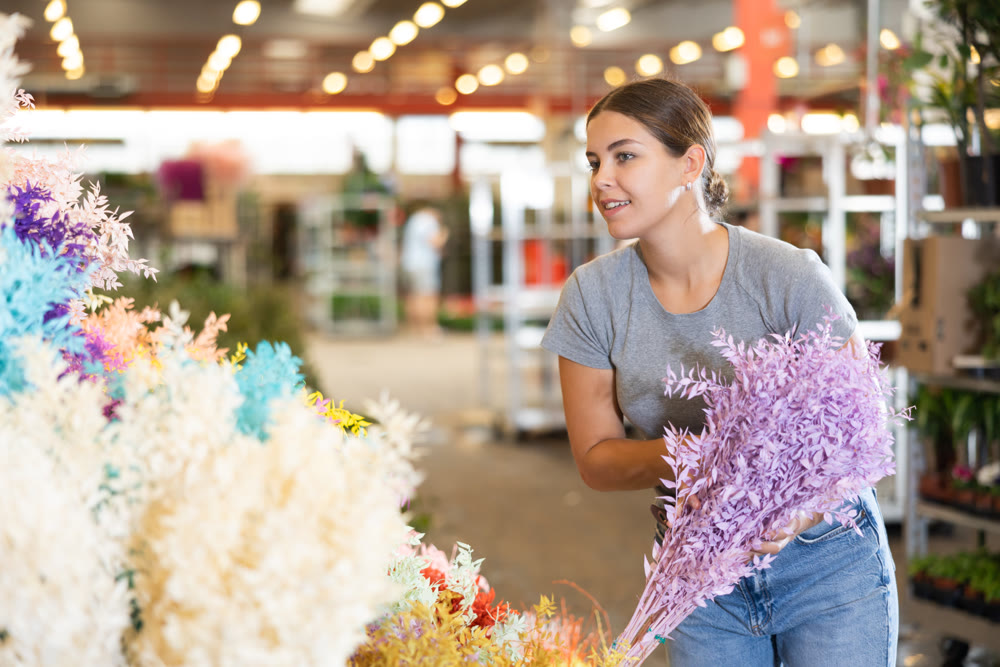 Young woman customer choosing bundle of dried ruscus in open-air plants market