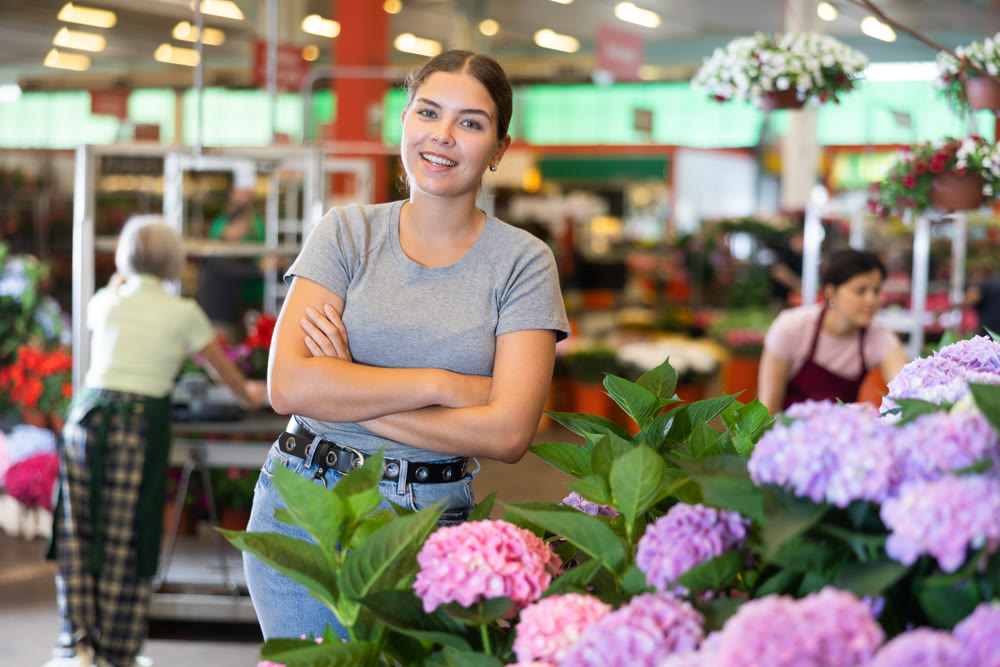 Young woman customer choosing bundle of hydrangea in open-air plants market