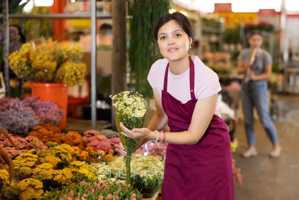 Portrait of a positive female flower market seller with bouquet of daisies for buyers