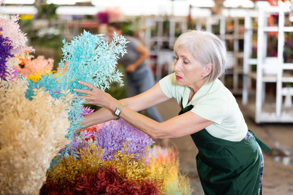 Old saleswoman placing bundle of dried ruscus in open-air plants market