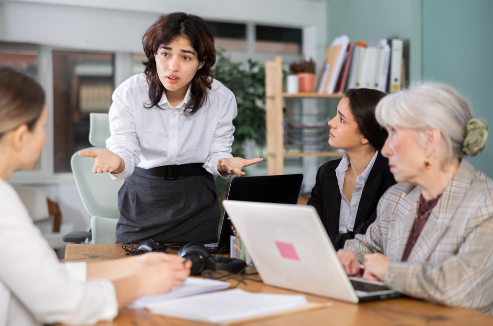 Young woman standing and scolding colleagues during stressful corporate meeting