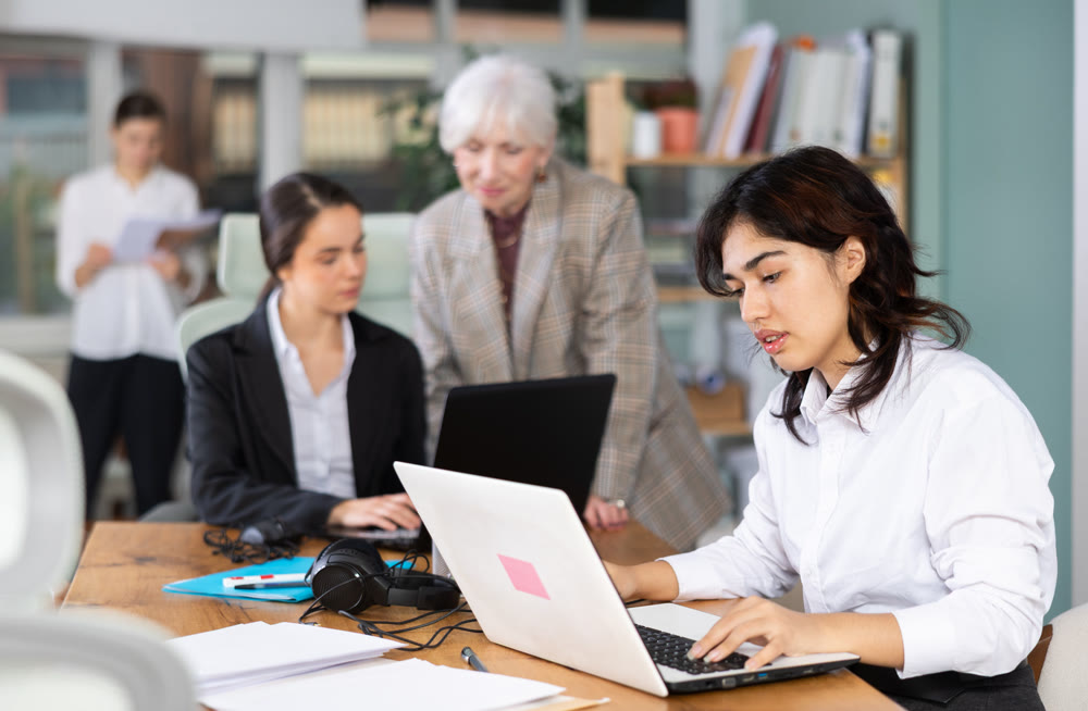Young woman works on laptop with female colleagues