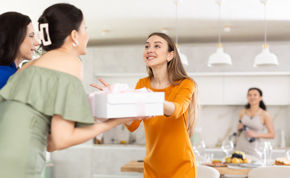 Excited woman hosting besties bringing gift for home get-together