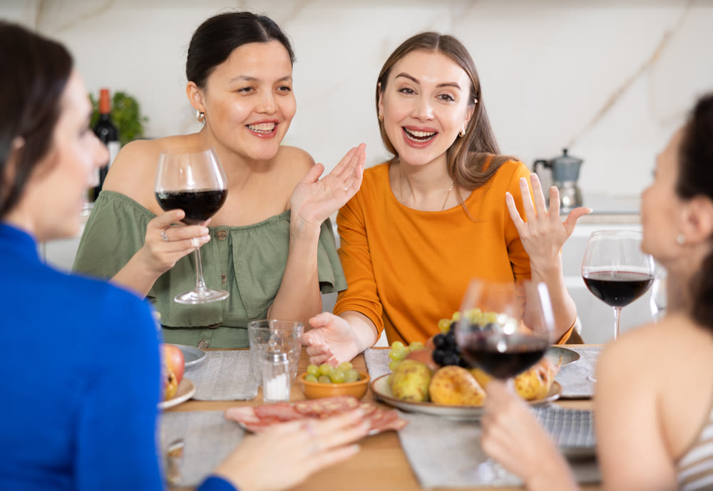 Girlfriends drinking wine and having conversation over dinner at house party