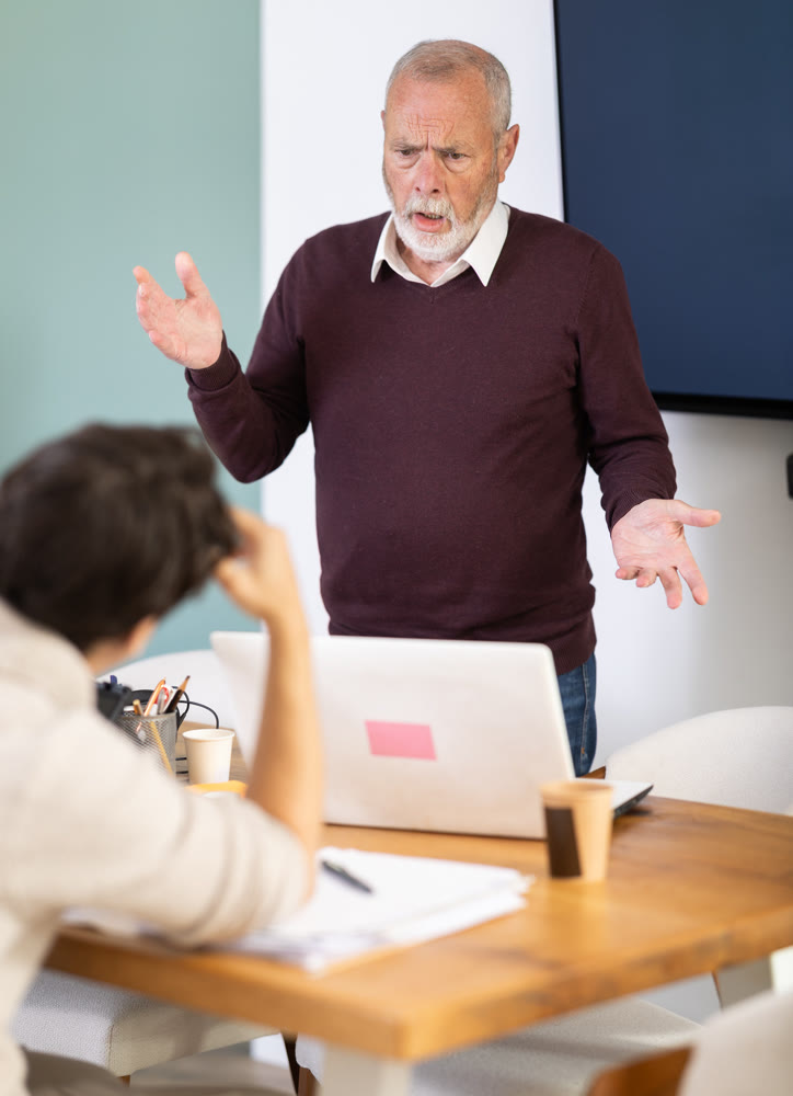 Senior man head of department shouts at guy subordinate who is working with documents