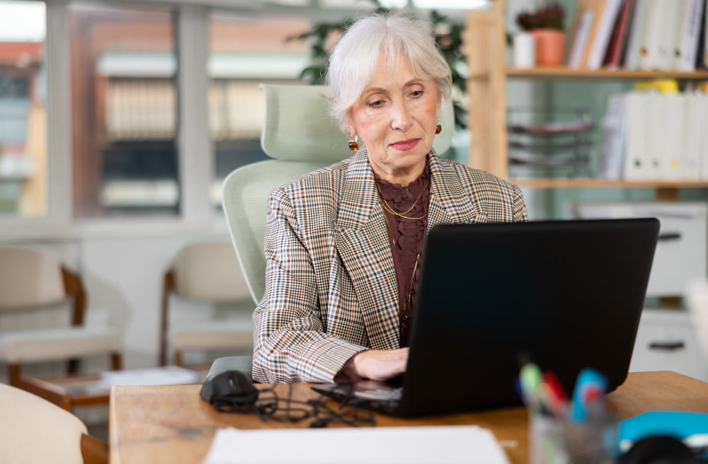 Elderly woman working on laptop in office