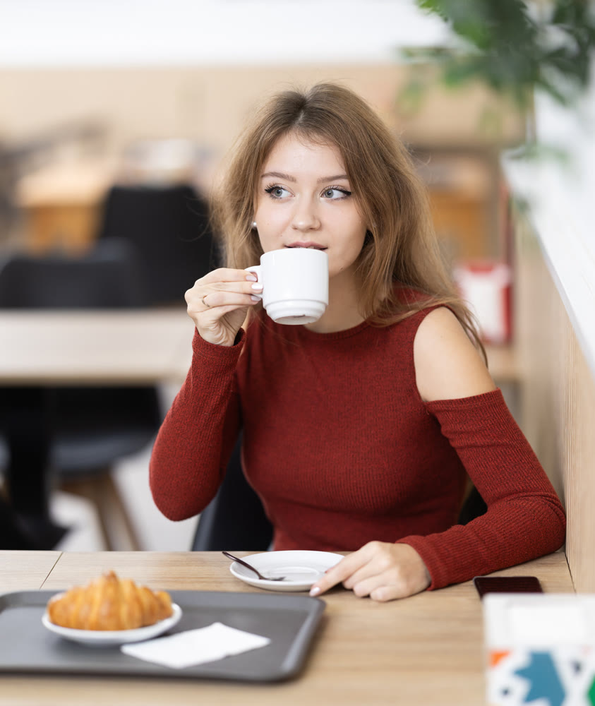 Young woman drinks coffee with croissant