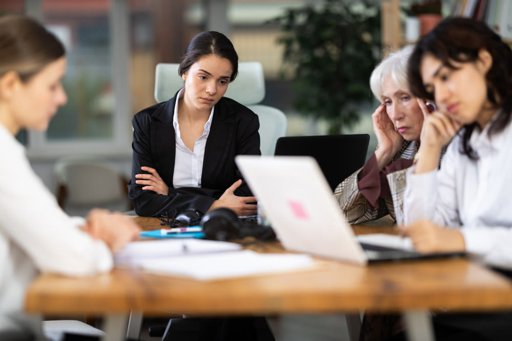 Tired Asian girl is sitting at computer at work in crowded office