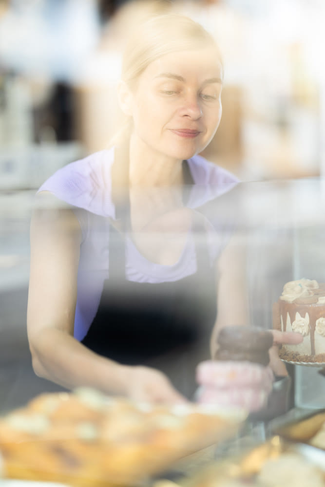 Young woman seller stands at bakery counter, present croissant