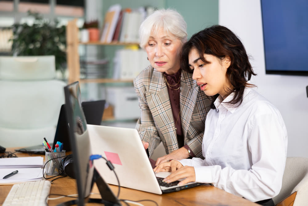 Elderly woman helping young woman with laptop