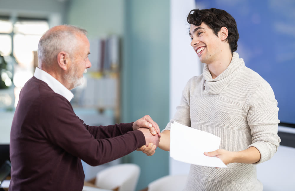 Smiling senior man makes deal, shaking hands with guy