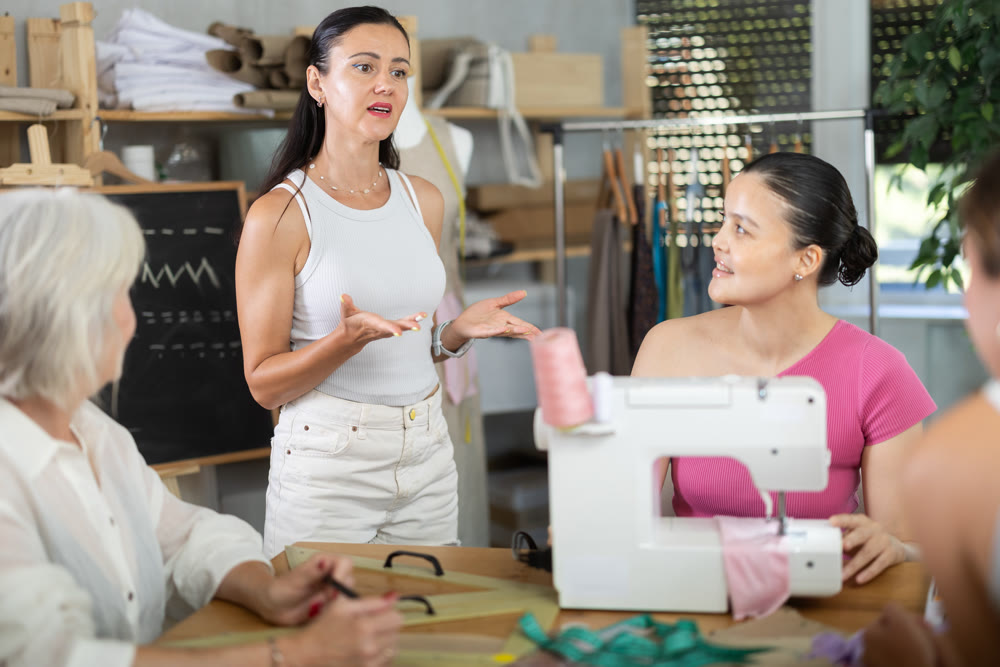 Experienced seamstress giving sewing lesson to group of female students