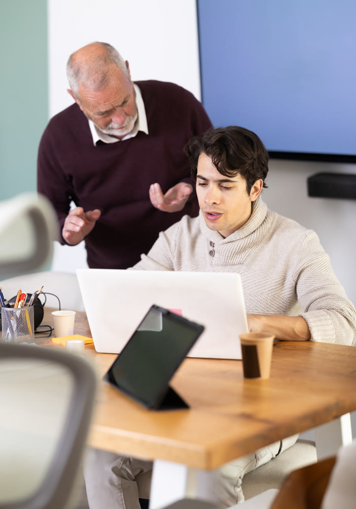 Senior man helps guy complete task on laptop