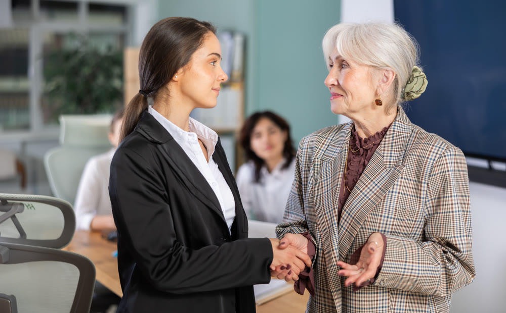Young and elderly woman shaking hands in office