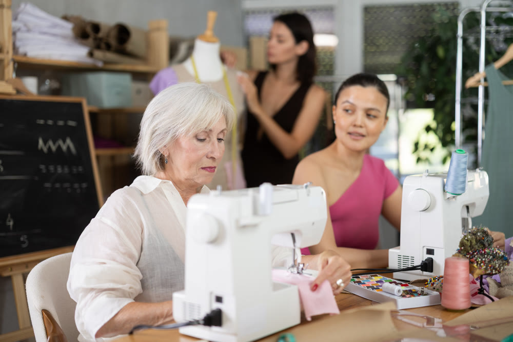 Mature woman stitching fabric on machine in sewing class for adults
