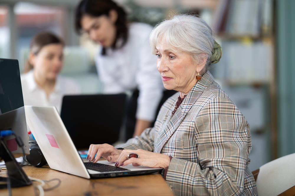 Elderly woman works on laptop with female colleagues