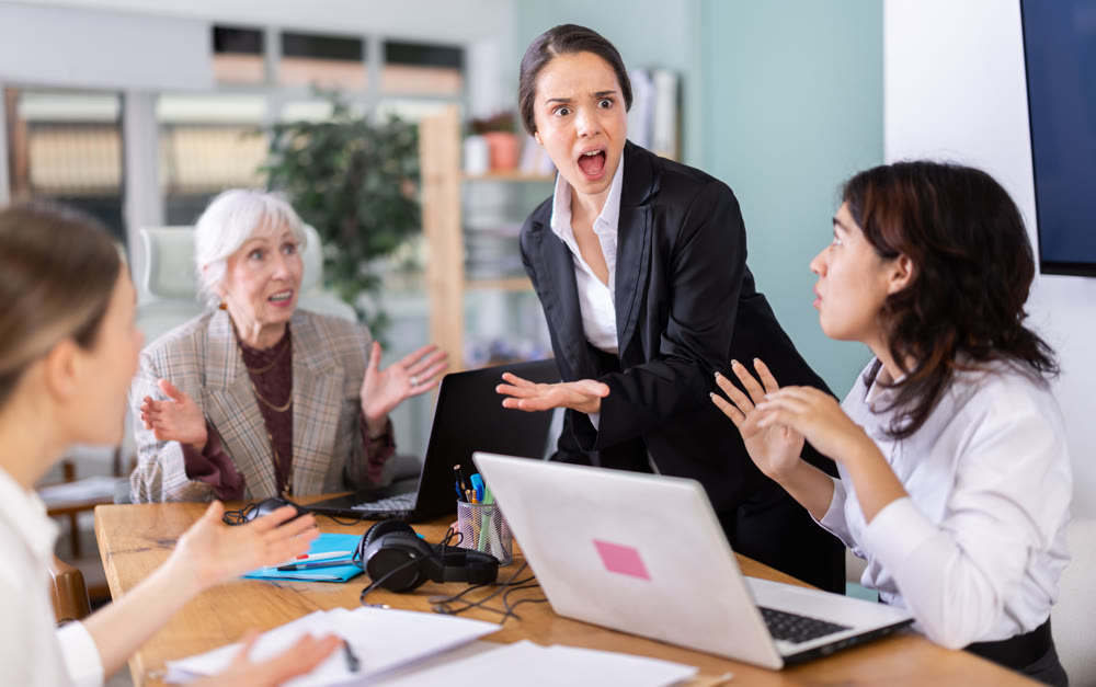 Young woman standing and scolding sad seated colleagues in office