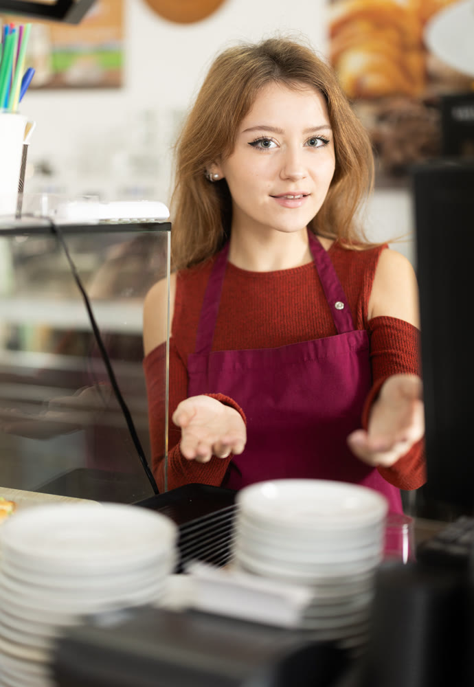 Positive female cafe employee puts clean plates on counter