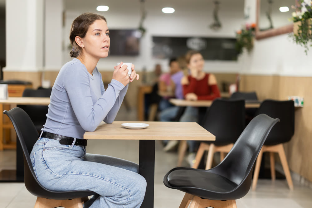 Lonely girl is sitting at table in cafe, drinking coffee