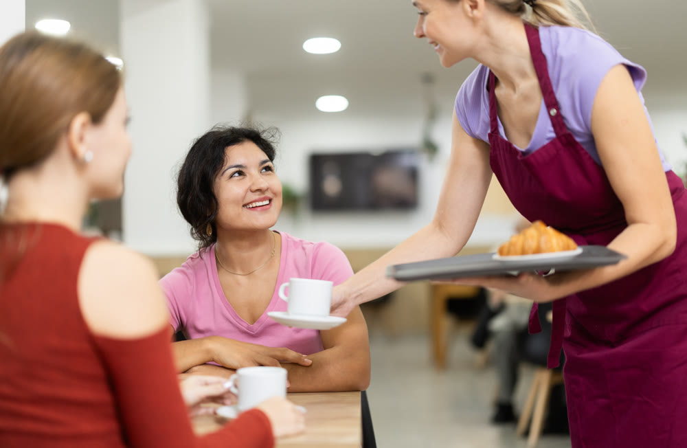 Adult female waitress serves coffee and croissant