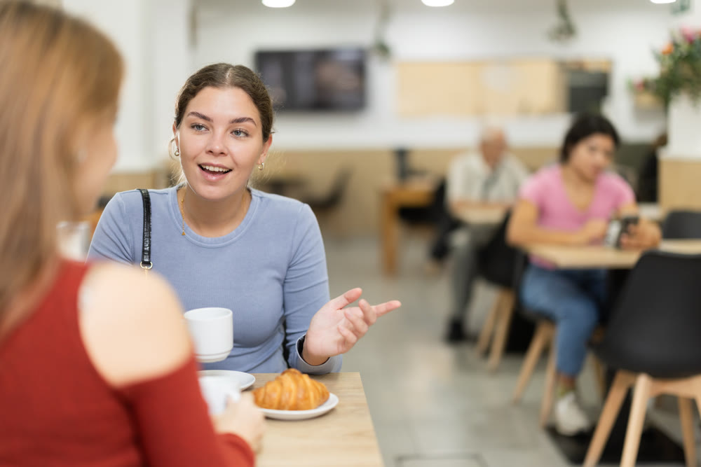 In cafe, girl chatting sweetly during tea party with girl buddy