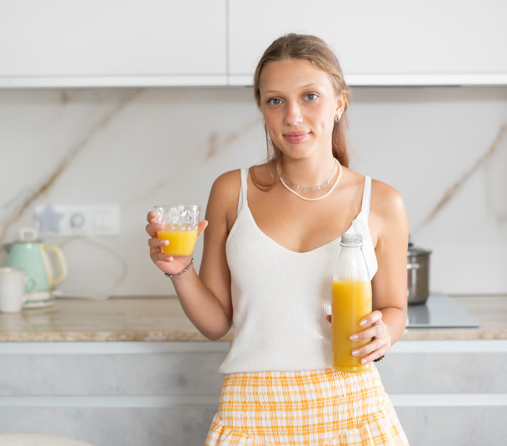 Young woman drinking freshly squeezed juice in kitchen