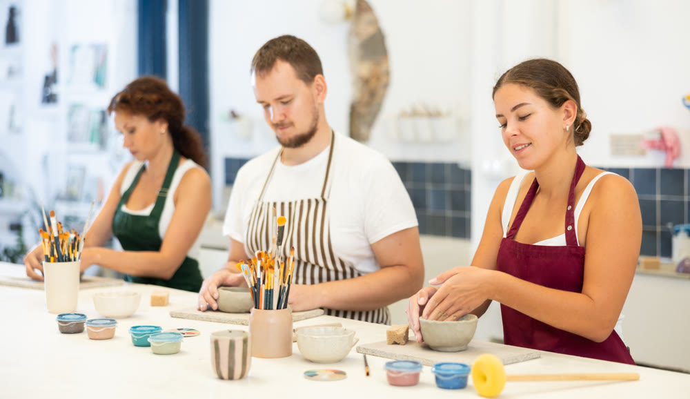 Three pottery workshop workers sculpt from raw clay