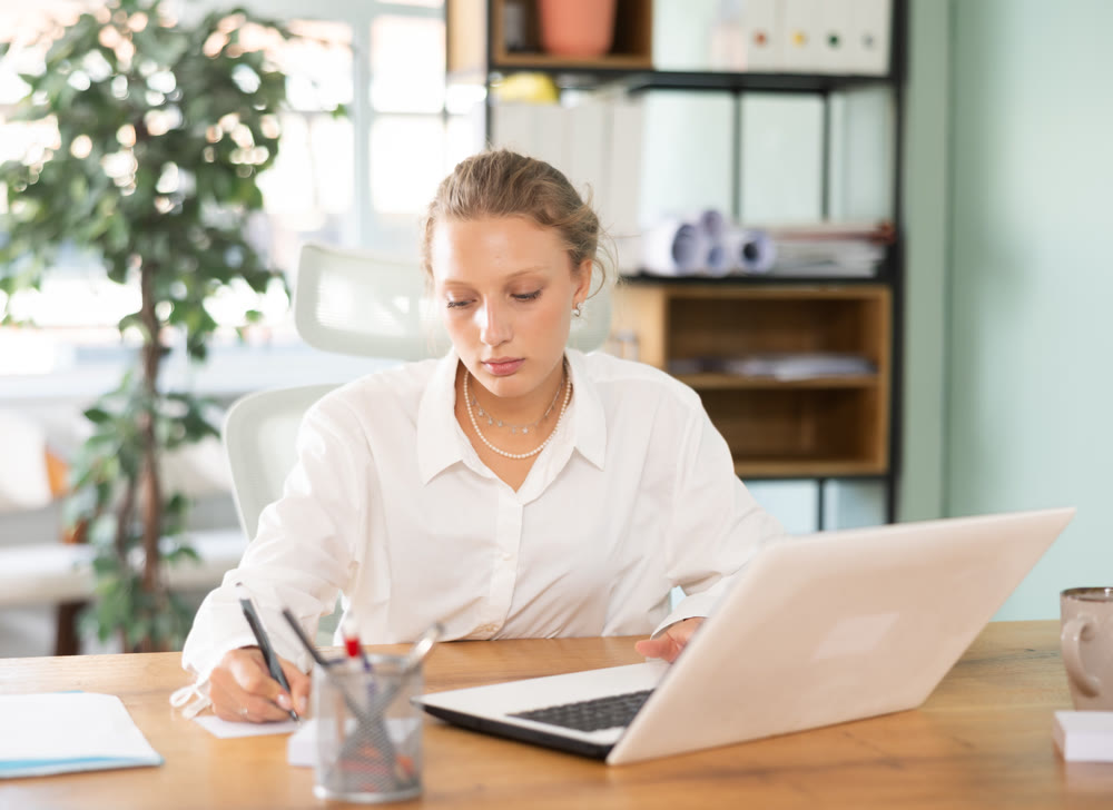 Young female manager in summer dress working on laptop sitting at desk in the office