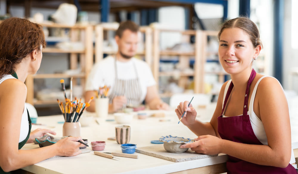 Pottery workers paint ceramic plates together at table