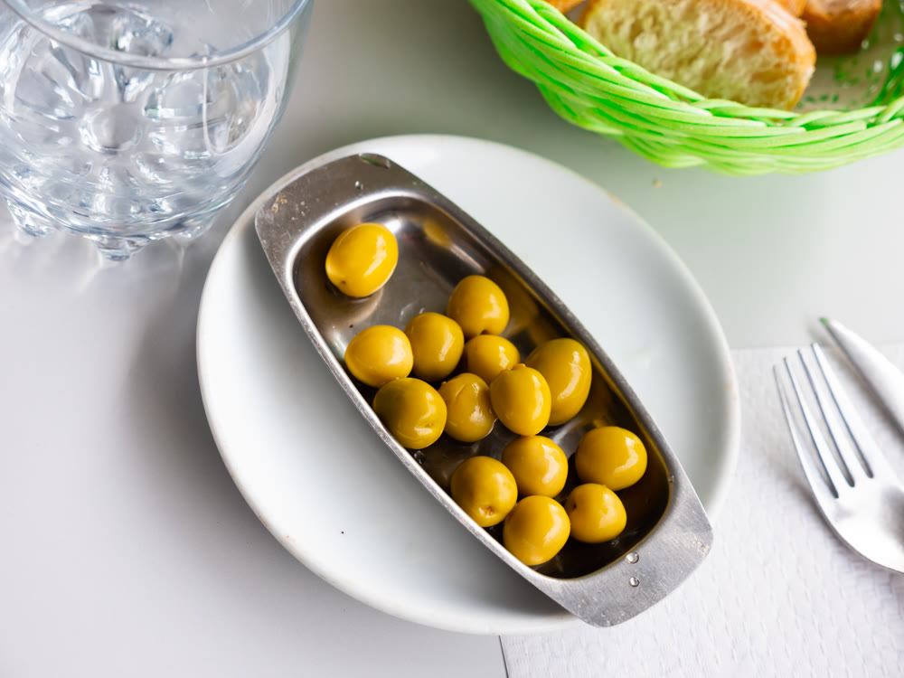 White plate with delicious green olives with pits closeup
