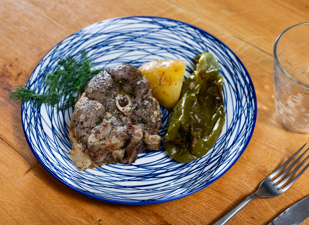 There are fried lamb ribs on plate. Meat appetizer is complemented with baked potatoes and bell peppers closeup