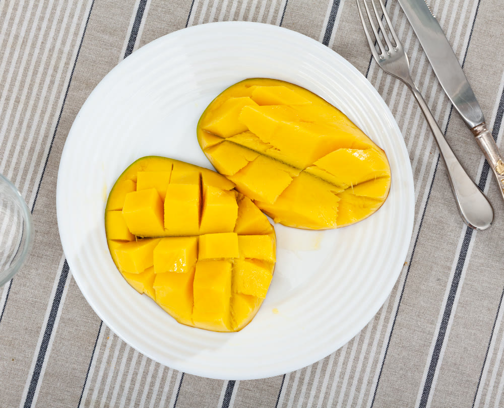Two halves of ripe yellow mango cut into cubes lie on white round plate