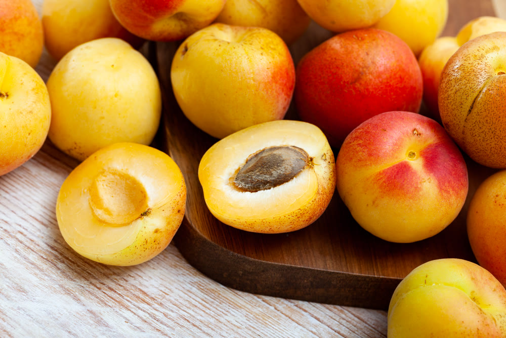 Whole and half fresh apricots on wooden table