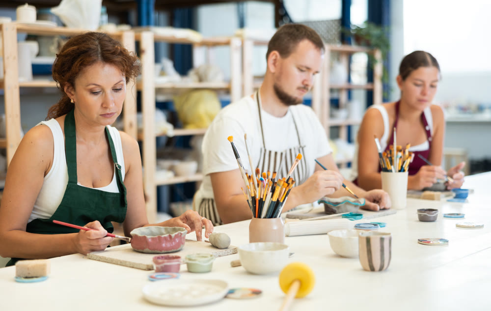 Three craftsperson are busy painting clay products