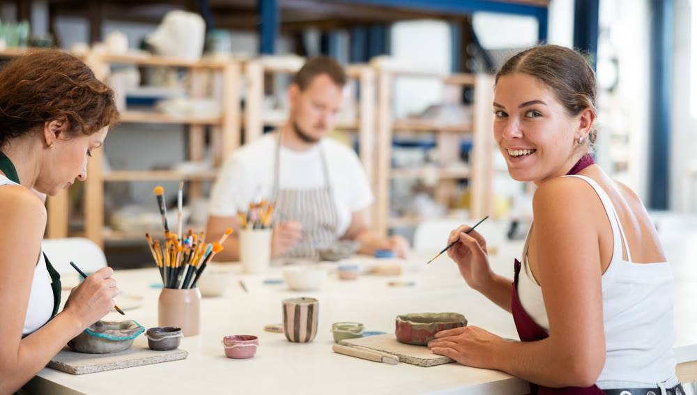 Pottery workers paint ceramic plates together at table