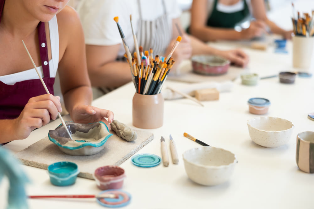 Close up girl paints bowl of clay during master class, top view.