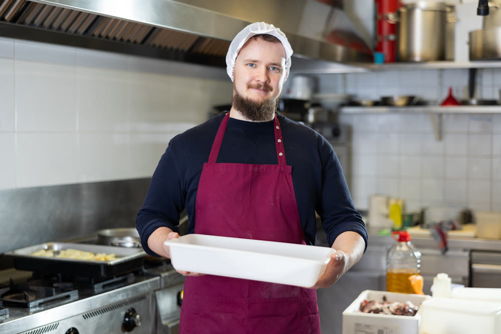 Bearded worker standing with empty tray in kitchen of deli department of store