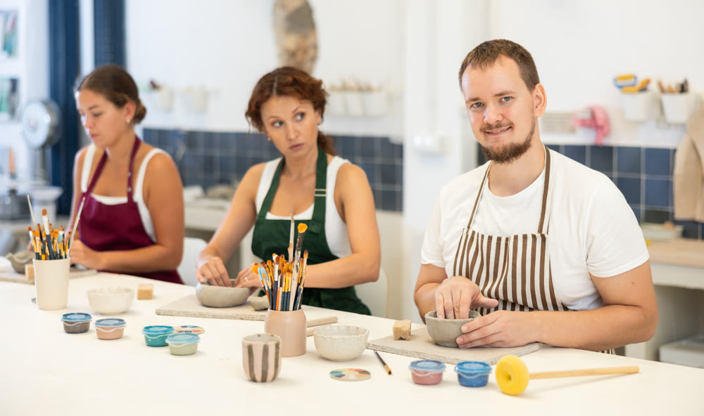 Three pottery workshop workers sculpt from raw clay