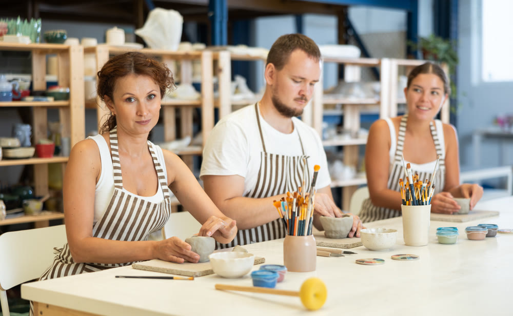 Three pottery workshop workers sculpt from raw clay