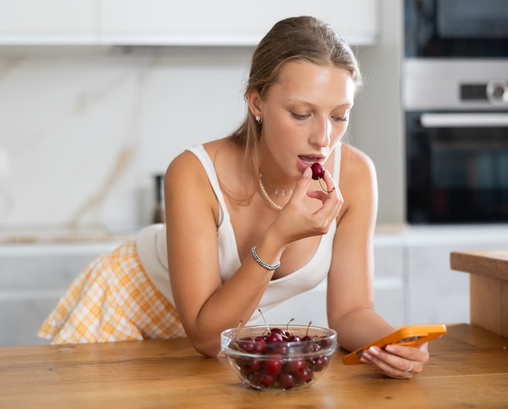 Happy young girl eating cherry in modern kitchen